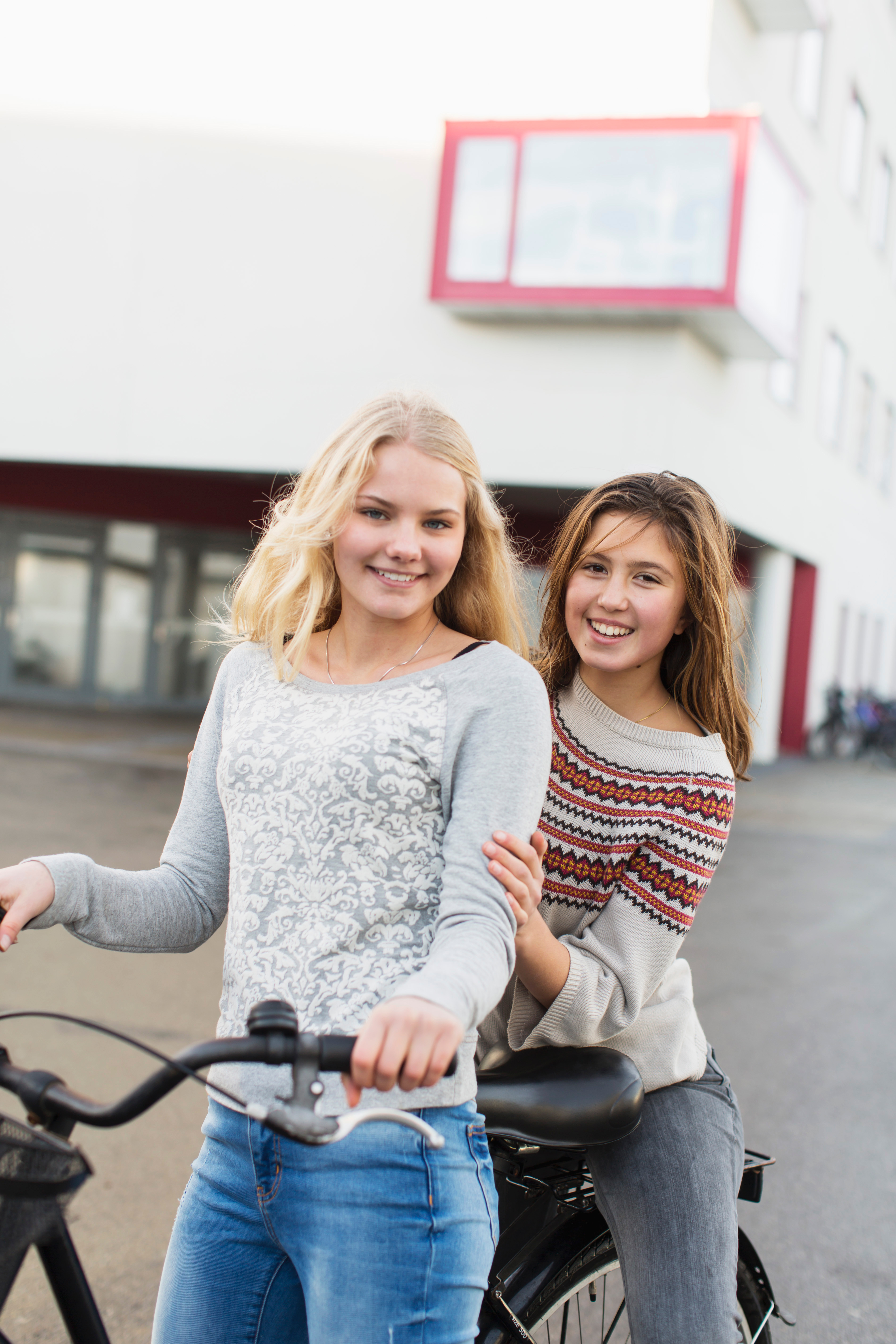 Zwei Schülerinnen stehen sich umarmend mit einem Fahrrad auf einem Parkplatz und lächeln in die Kamera.